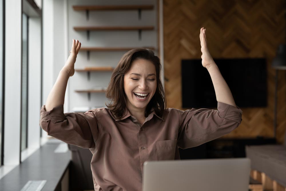 Överlycklig ung kvinna som tittar på bärbar datorskärm och firar